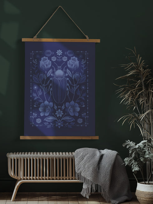 A symmetrical wall tapestry in monochromatic navy blue featuring a detailed scarab beetle surrounded by flowers and botanical elements, mounted on a wooden dowel with natural twine.